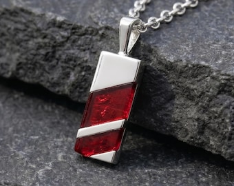 May include: A silver pendant necklace featuring a rectangular design with a polished silver top and bottom section and a textured, deep red glass inlay in the center, suspended from a matching silver chain link necklace.