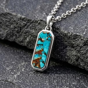 May include: A rectangular pendant necklace featuring a vibrant turquoise stone with brown matrix patterns set in a polished silver-toned metal frame, suspended from a matching silver-toned chain link necklace with a secure bail attachment.
