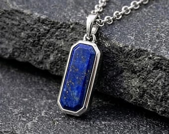 May include: A rectangular pendant necklace featuring a deep blue lapis lazuli stone with gold-colored flecks, set in a polished silver-toned metal frame. The pendant hangs from a matching silver-toned metal chain with small, rounded interlocking links.