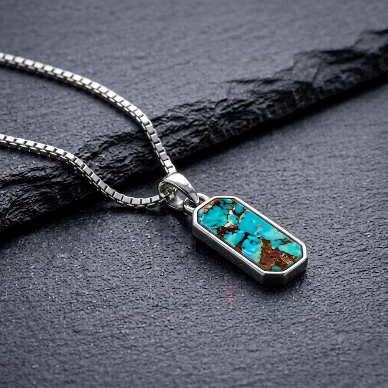 May include: A silver box chain necklace featuring a rectangular pendant with a polished silver frame. The pendant is inlaid with a vibrant turquoise stone that displays a natural matrix of bright blue and deep brown earthy mineral veins.