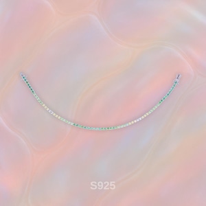 Peut inclure: Un bracelet en argent délicat avec une rangée de petites pierres précieuses taillées en carré qui passent du vert au jaune. Le bracelet est incurvé et possède un fermoir. Le texte "S925" est visible.