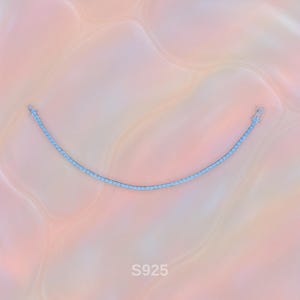 Puede incluir: Un delicado brazalete de tenis plateado con un diseño curvo. El brazalete está adornado con pequeñas piedras brillantes. El fondo es una suave mezcla abstracta de tonos rosa y melocotón. El texto "S925" es visible.