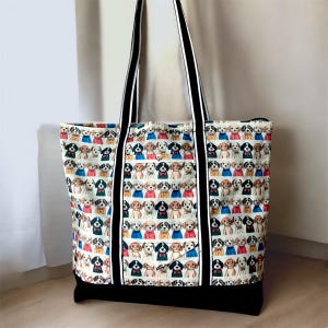 May include: A large tote bag featuring a repeating pattern of cartoon dogs in different outfits. The bag has black and white striped handles and a solid black base. The background is a neutral colour.