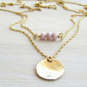 May include: A gold chain necklace with a hammered gold disc pendant and a row of three light pink beads.