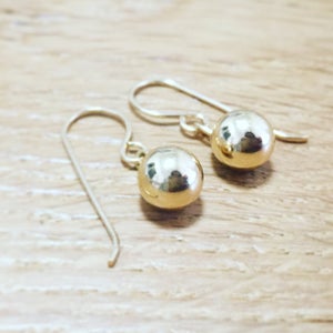 May include: A pair of gold ball drop earrings with a simple design. The earrings are made of gold metal and have a smooth, shiny finish.