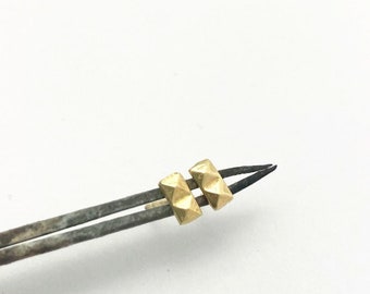May include: Two gold-colored pyramid-shaped beads are attached to a pair of tweezers.