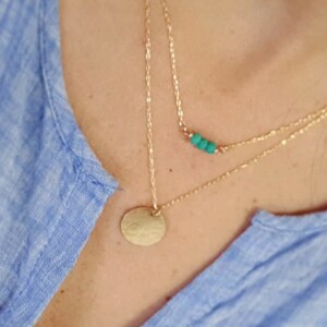 May include: A layered gold necklace with a small turquoise bead bar and a larger round pendant.