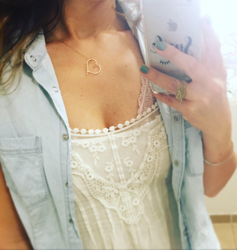 May include: A woman wearing a light blue denim shirt over a white lace top with a delicate gold heart necklace.
