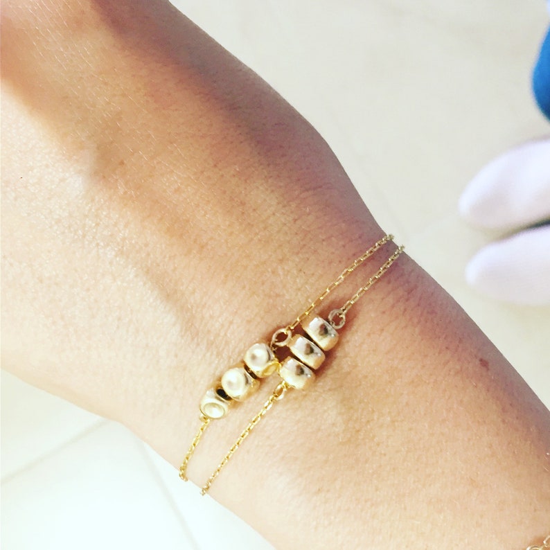 K&ouml;nnte beinhalten: Ein goldenes Kettenarmband mit einer Reihe kleiner, runder goldener Perlen.