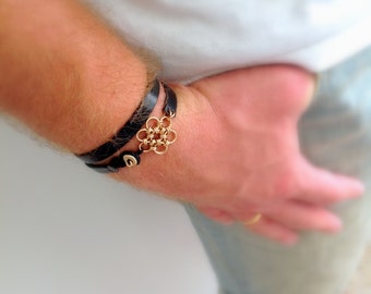 May include: A black leather bracelet with a gold metal charm in the shape of a flower.