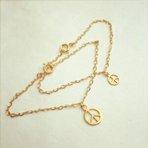 May include: A gold chain bracelet with two peace sign charms. The bracelet is made of a delicate chain and the charms are small and simple.
