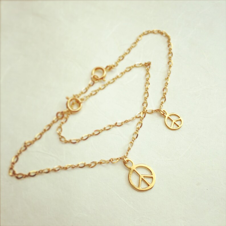 May include: A gold chain bracelet with two peace sign charms. The bracelet is made of a delicate chain and the charms are small and simple.