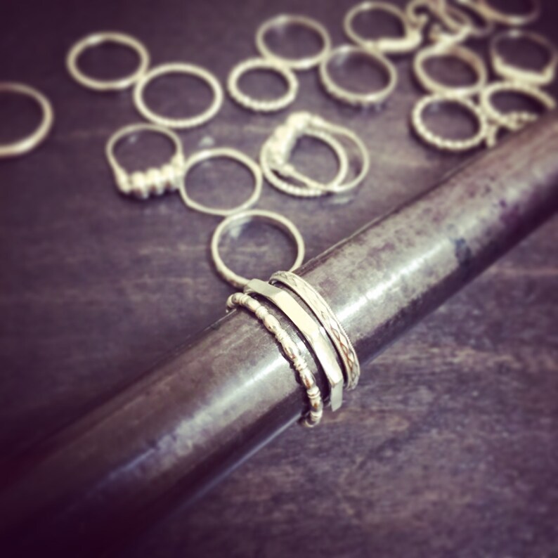 May include: A close-up of a silver metal rod with four silver rings stacked on it. The rings are of different widths and have various textures.