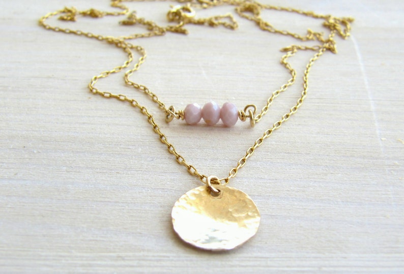 May include: A gold chain necklace with a hammered gold disc pendant and a row of three light pink beads.