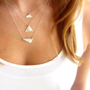 May include: A layered silver necklace with three triangle pendants of varying sizes. The necklace is worn by a person with long, light brown hair.