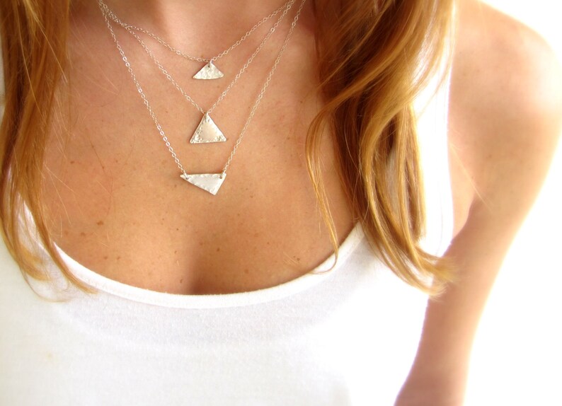 May include: A layered silver necklace with three triangle pendants of varying sizes. The necklace is worn by a person with long, light brown hair.