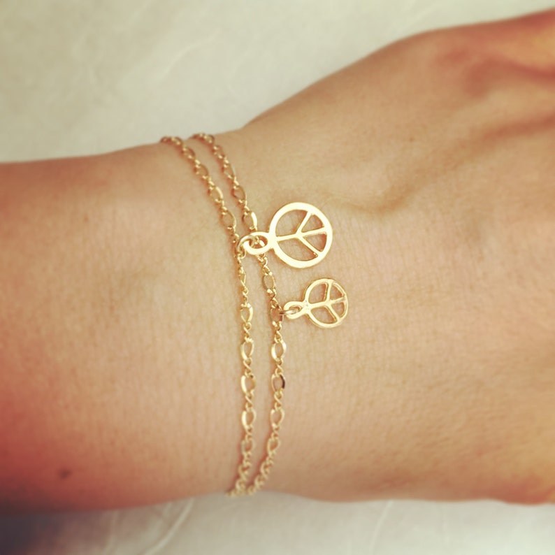May include: A gold chain bracelet with two peace sign charms. The bracelet is layered and has a delicate chain.