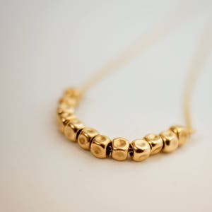 Puede incluir: Un collar de oro con una cadena y una fila de cuentas redondas texturizadas.