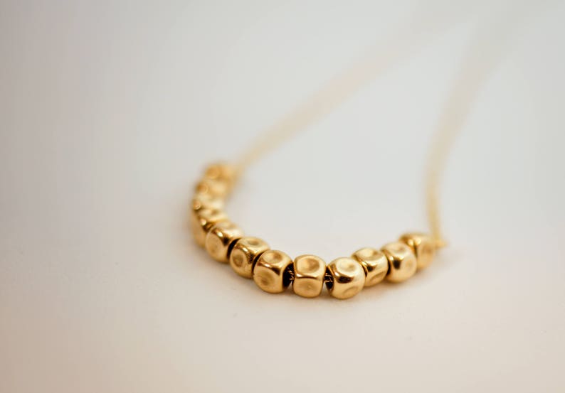Puede incluir: Un collar de oro con una cadena y una fila de cuentas redondas texturizadas.
