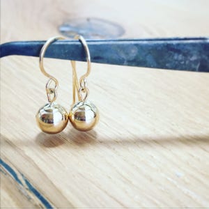 May include: A pair of gold ball drop earrings. The earrings are made of gold and have a simple design.