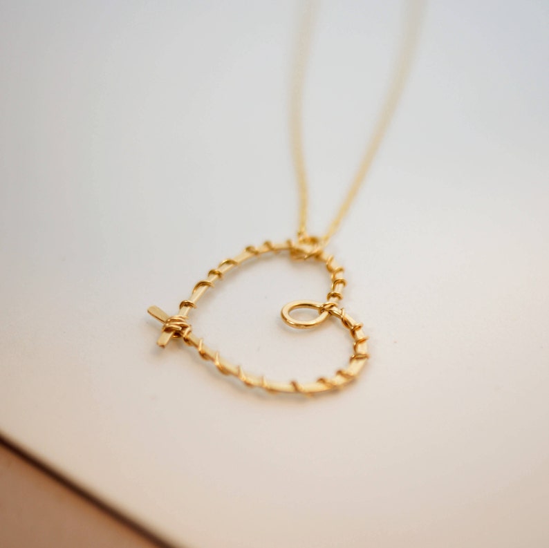 May include: A gold necklace with a heart-shaped pendant made of twisted wire. The pendant has a small circle in the center.