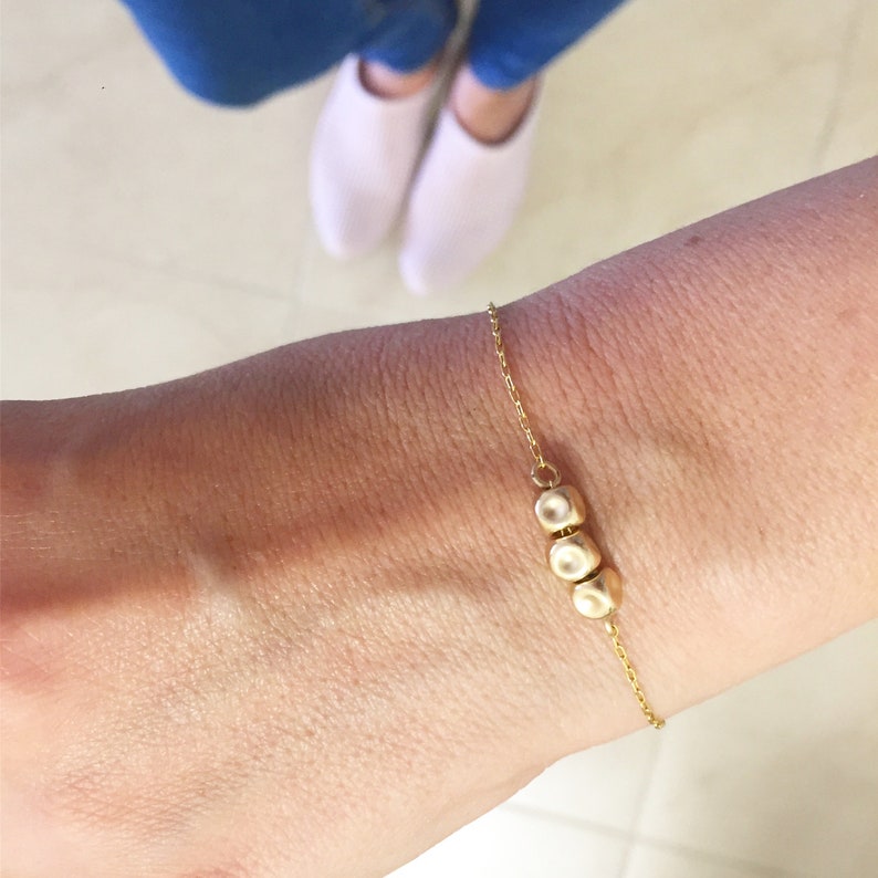 K&ouml;nnte beinhalten: Ein goldenes Kettenarmband mit drei runden goldenen Perlen.