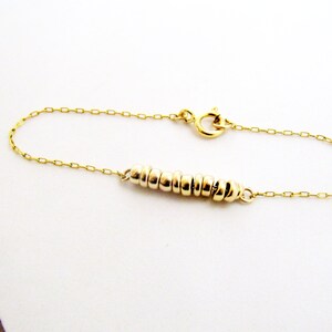 May include: A gold chain bracelet with a delicate chain and a row of small gold rings.