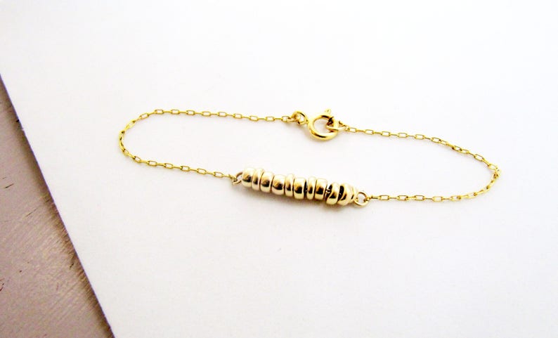 May include: A gold chain bracelet with a delicate chain and a row of small gold rings.