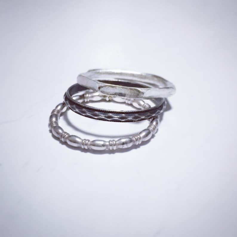 May include: Three silver rings stacked on top of each other. The top ring is plain, the middle ring has a textured design, and the bottom ring has a beaded design.