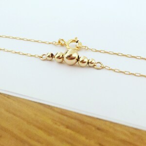 Puede incluir: Un delicado collar de oro con una serie de peque&ntilde;as cuentas redondas de varios tama&ntilde;os. Las cuentas est&aacute;n agrupadas en el centro de la cadena, con una cuenta m&aacute;s grande como punto focal. El collar tiene un cierre sencillo.