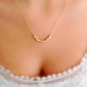 Puede incluir: Un collar de oro con una cadena delicada y una fila de peque&ntilde;as cuentas cuadradas. El collar lo lleva una persona con una camisa blanca.