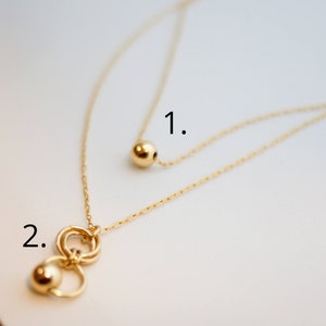 May include: Two gold necklaces with different pendants. The first necklace has a single round pendant. The second necklace has a pendant with three interlocking circles and a round bead.
