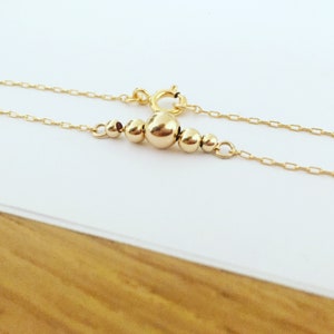 Puede incluir: Un delicado collar de oro con una serie de peque&ntilde;as cuentas redondas de varios tama&ntilde;os. Las cuentas est&aacute;n agrupadas en el centro de la cadena, con una cuenta m&aacute;s grande como punto focal. El collar tiene un cierre sencillo.