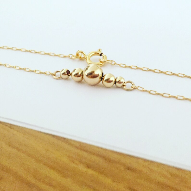 Puede incluir: Un delicado collar de oro con una serie de peque&ntilde;as cuentas redondas de varios tama&ntilde;os. Las cuentas est&aacute;n agrupadas en el centro de la cadena, con una cuenta m&aacute;s grande como punto focal. El collar tiene un cierre sencillo.