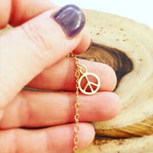 May include: A gold chain necklace with a peace sign charm. The chain is delicate and the peace sign is small.
