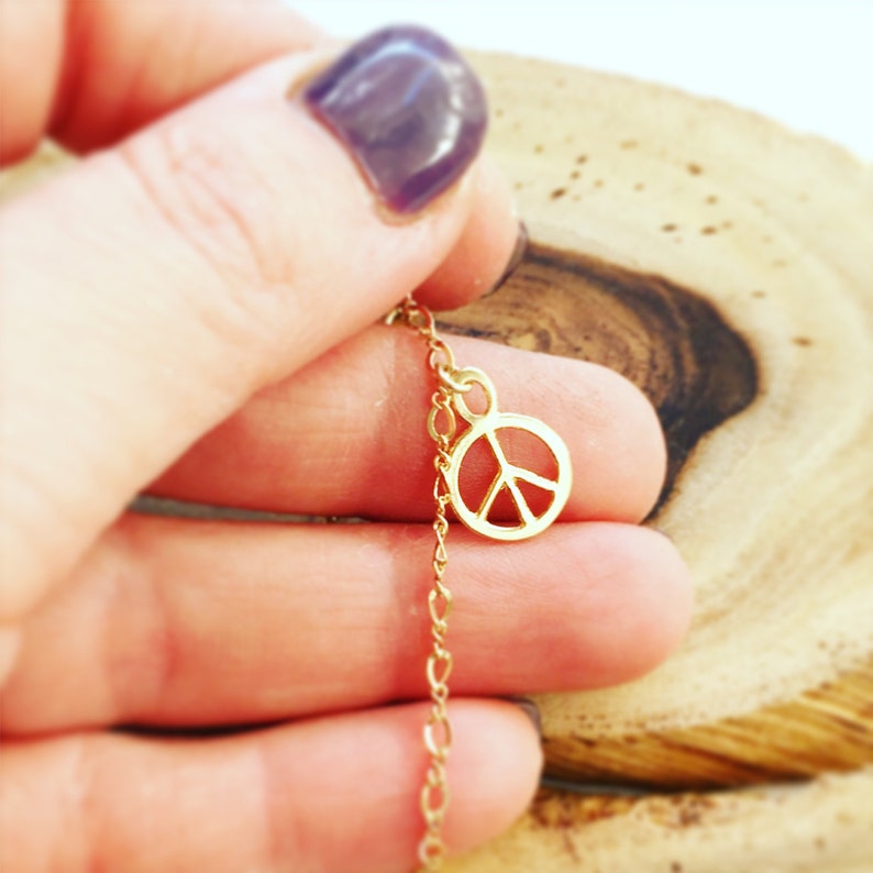 May include: A gold chain necklace with a peace sign charm. The chain is delicate and the peace sign is small.