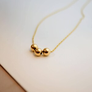 May include: A gold necklace with three round beads.