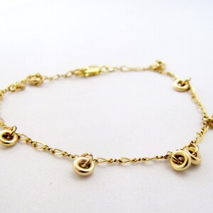 May include: A delicate gold bracelet with small, round charms evenly spaced along a fine chain. The bracelet has a simple clasp and is set against a white background. The jewelry is a classic and elegant accessory.