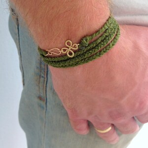 May include: A green braided bracelet with a gold charm on a person's wrist.