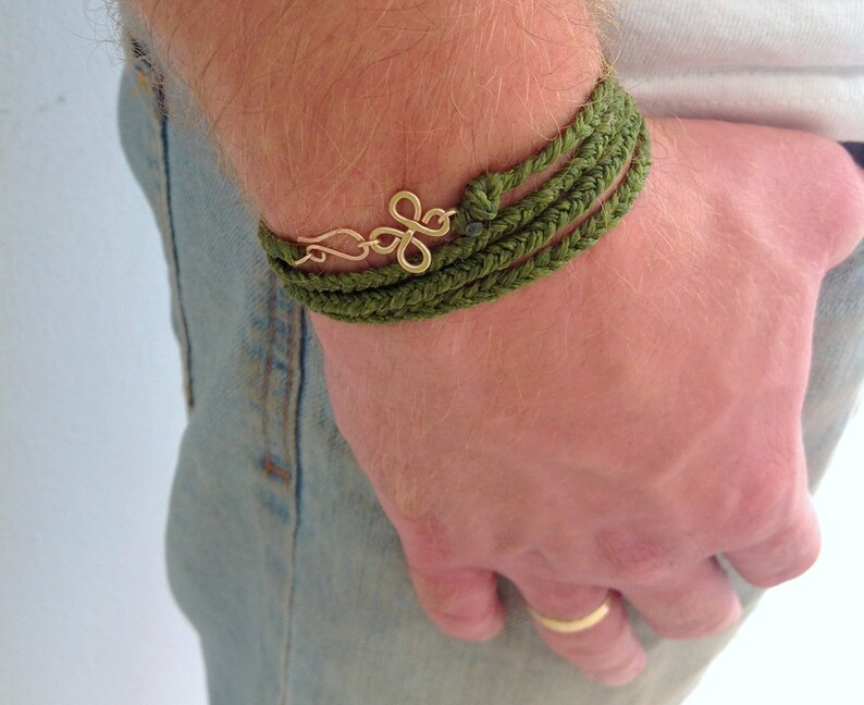 May include: A green braided bracelet with a gold charm on a person's wrist.