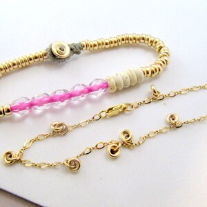 May include: Two bracelets. One is gold-colored with small beads and a gray clasp. The other is a gold chain with spiral charms and a clasp. The first bracelet has pink and clear beads.