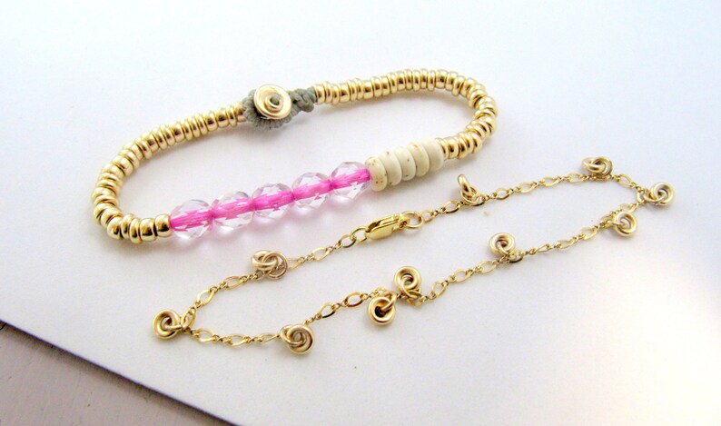 May include: Two bracelets. One is gold-colored with small beads and a gray clasp. The other is a gold chain with spiral charms and a clasp. The first bracelet has pink and clear beads.