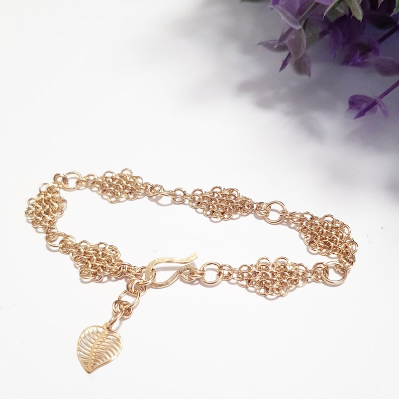 May include: A gold bracelet with a delicate chain and a leaf charm. The bracelet is made of small, interconnected rings that create a unique and intricate design.