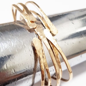 Puede incluir: Un conjunto de cuatro pulseras de metal martillado de color dorado. Las pulseras est&aacute;n apiladas una encima de la otra y tienen una forma ligeramente irregular.