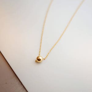 May include: A delicate gold chain necklace with a single, round gold bead pendant.