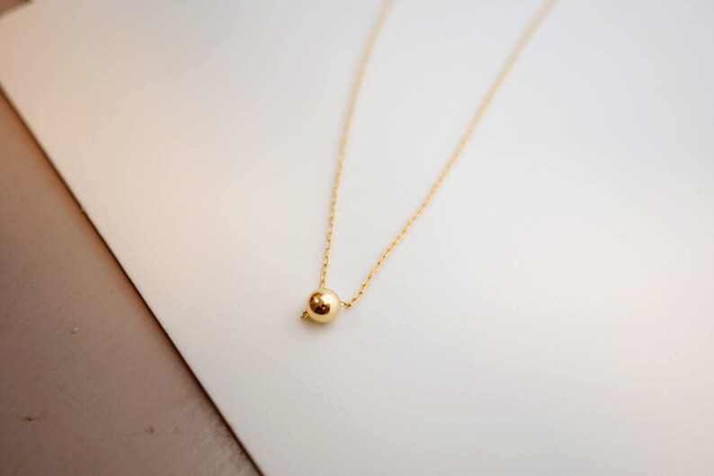 May include: A delicate gold chain necklace with a single, round gold bead pendant.