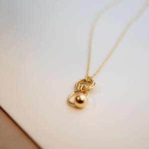 May include: A gold necklace with a pendant featuring a circle design with a smaller sphere attached.