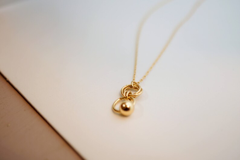 May include: A gold necklace with a pendant featuring a circle design with a smaller sphere attached.