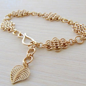 May include: A gold chain bracelet with a leaf charm. The bracelet is made of multiple chain links and has a lobster clasp closure.