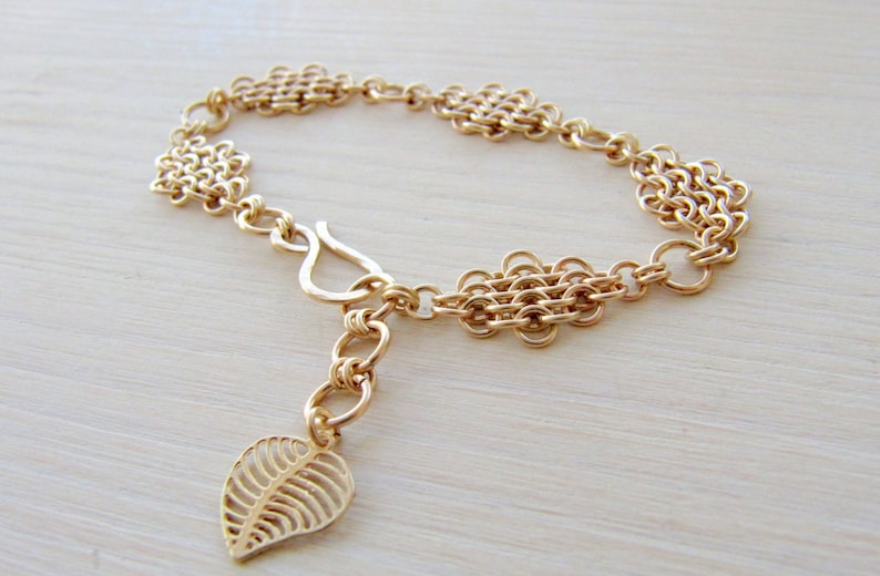 May include: A gold chain bracelet with a leaf charm. The bracelet is made of multiple chain links and has a lobster clasp closure.